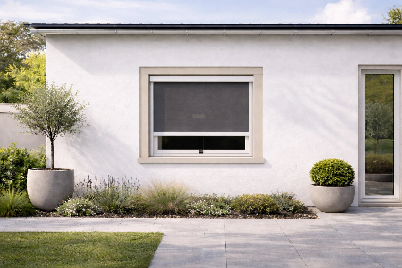 Außenansicht einer modernen Fassade mit Garten. Am Fenster ist das Außenrollo zum klemmen montiert und halb geschlossen.